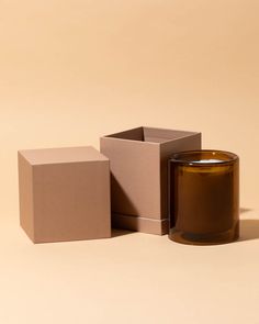 a candle sitting next to a box on a table with a light brown surface in the background