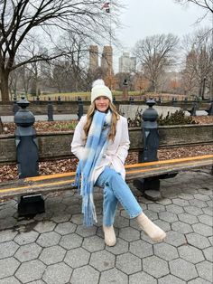 a woman sitting on a park bench wearing a blue scarf and white boots with her hands in her pockets