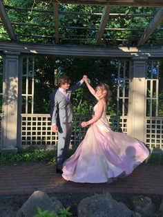 a young man and woman in formal wear dancing under a pergolated gazebo