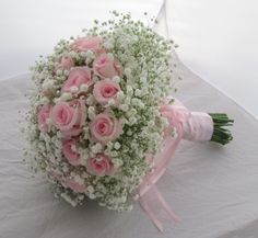 a bouquet of pink roses and baby's breath sits on a white tablecloth