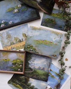 some paintings are laying on a table with flowers and plants around them, including water lilies