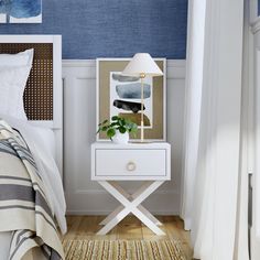 a white nightstand with a plant on it in front of a blue wall and bed