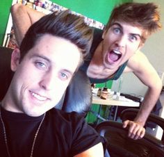 two young men posing for the camera in front of a green wall and black chair