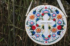 a cross hanging from a tree with flowers and leaves on it's side, in front of bamboo trees