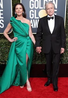 an older man and woman in formal wear walking down the red carpet at golden globe awards