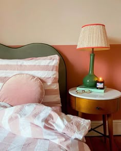 a bed with pink and white sheets, a green lamp and a wooden night stand