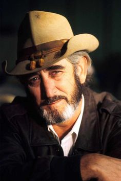 an older man wearing a cowboy hat with his arms crossed and looking at the camera