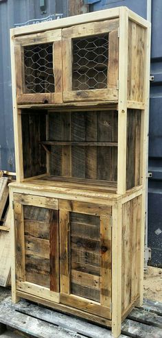 a wooden cabinet sitting on top of pallets in front of a metal container with chicken wire