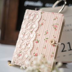 a close up of a small card holder on a table with flowers and a clock in the background