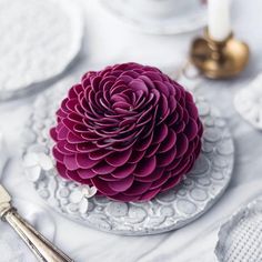 a white plate topped with a purple flower on top of a table next to silverware