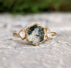 a close up of a ring on top of a stone surface with green plants in the background