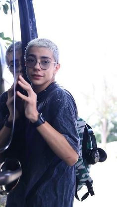 a man with glasses is looking at his cell phone while standing in front of a bus