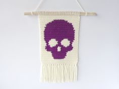 a crocheted wall hanging with a purple skull on the front and white background