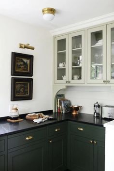 a kitchen with green cabinets and black counter tops, gold pulls on the cupboards