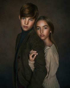 a boy and girl are posing for a portrait in front of a dark background, one is holding the other's arm