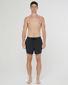 a man standing in front of a white background wearing black swim trunks and no shirt