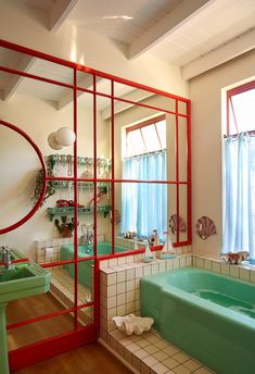 a bathroom with a green tub and red trim around the window, along with shelves on the wall