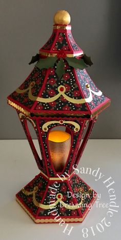 a red and gold lit candle holder on a white table top with a gray background