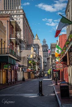 an empty city street with buildings and flags flying in the wind on a sunny day