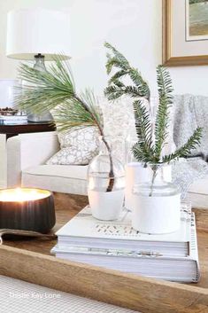 a coffee table with candles, books and plants on it in front of a couch