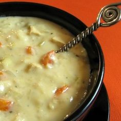 a black bowl filled with soup on top of an orange cloth covered table next to a silver spoon