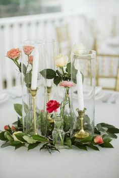 flowers and candles are arranged in glass vases on a white tablecloth with greenery