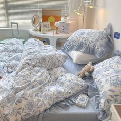 an unmade bed with blue and white comforters, pillows and a teddy bear