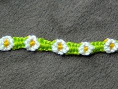 a crocheted bracelet with white flowers on green and yellow yarn, sitting on a gray surface