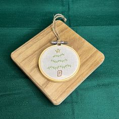 a cross stitch ornament hanging from a wooden frame on a green fabric background