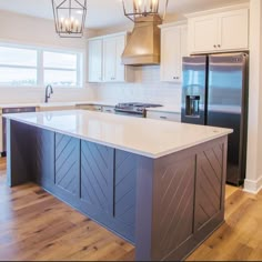 a large kitchen with an island in the middle and two lights hanging from the ceiling