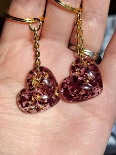 two heart shaped glass beads are being held in someone's hand with gold chains