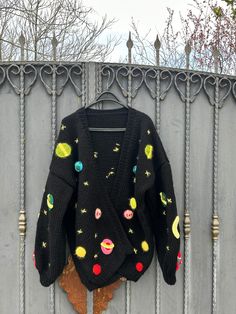 a sweater hanging on a metal fence with space and planets all over it, in front of a tree