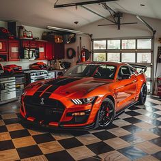 an orange sports car in a garage with checkerboard flooring and red cabinets