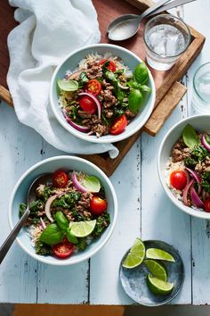 three bowls filled with meat and vegetables on top of a wooden table next to water