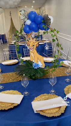 the lion king centerpiece is surrounded by blue and gold table linens, silverware, and balloons