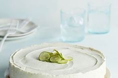 a white cake with limes on top sitting on a table next to glasses and plates