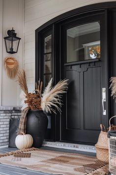 Black front door with large window, surrounded by autumn decor including dried plants in a black vase, a white pumpkin, and woven baskets. Chic Fall Front Door Decor, Minimal Fall Decor Porch, Modern Farmhouse Fall Decor Front Porch, Fall Outside Decor, Minimal Fall Decor, Modern Farmhouse Fall Decor, Fall Patio Decor, Throw Pillows And Blankets, Fall Entryway Decor