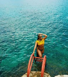 a woman in a yellow shirt is sitting on a red chair by the water's edge