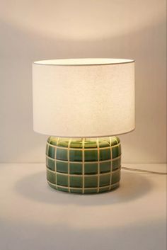 a green table lamp with a white lampshade sitting on the floor next to it