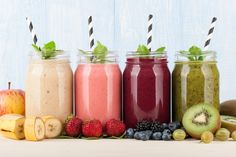 four jars filled with different types of smoothies and fruit on top of a table