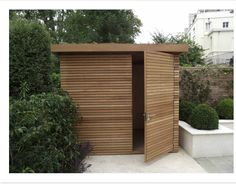 a small wooden structure in the middle of a garden with shrubbery and bushes around it