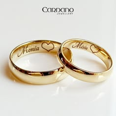 two gold wedding rings with hearts and names on them, sitting next to each other