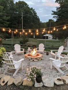 a fire pit surrounded by lawn chairs and string lights in the backyard with rocks around it