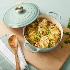 a casserole dish with chicken and vegetables on a cutting board next to a wooden spoon