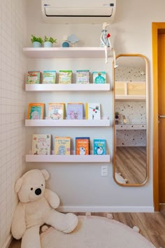 a teddy bear sitting on the floor in front of a bookshelf with children's books