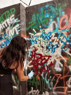 a woman is painting graffiti on a wall with spray paint and blue gloves in front of her