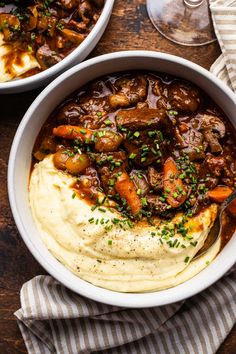 two bowls filled with mashed potatoes and beef stew on top of a wooden table