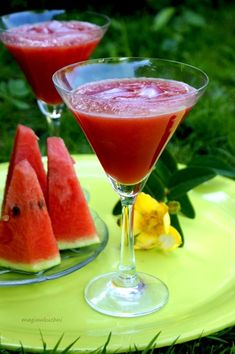 two glasses filled with watermelon juice on top of a yellow plate in the grass