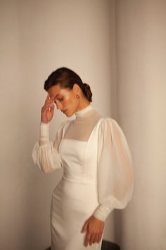 a woman in a white dress is holding her hand up to her face and looking down