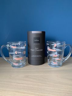 two glass mugs sitting next to each other on a wooden table with a blue wall in the background